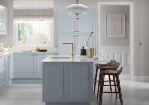 Modern kitchen with light blue cabinets, island, bar stools, and natural light from a window.