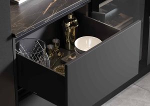 Open kitchen drawer with plates, glasses, and a gold cocktail shaker inside.