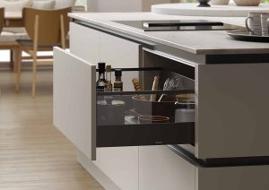 A modern kitchen drawer partially open, displaying utensils and kitchen items inside.