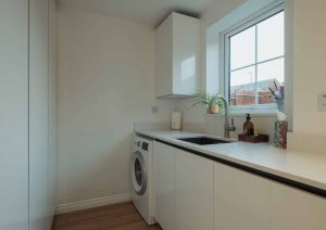 Modern laundry room with white cabinets, a washing machine, and a window above the sink.