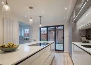 Modern kitchen with white countertops, island, pendant lights, and glass doors leading to a patio.