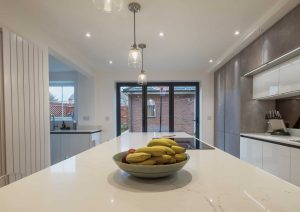Modern kitchen with a bowl of bananas on a white countertop, large windows in the background.