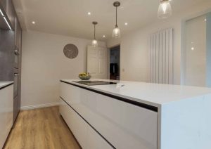 Modern kitchen with white cabinets, a large island, and wooden floors under pendant lights.