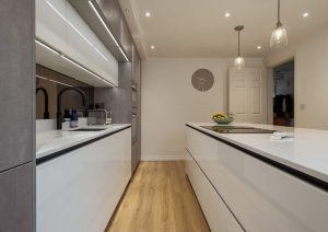Modern kitchen with white cabinets, island countertop, wooden floor, and pendant lights.