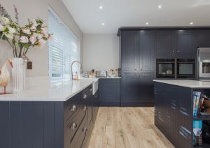 Modern kitchen with dark cabinets, light countertops, and wooden flooring.
