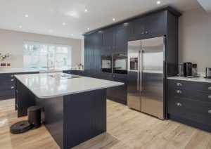 Modern kitchen with dark cabinets, large island, stainless steel fridge, and wooden floors.