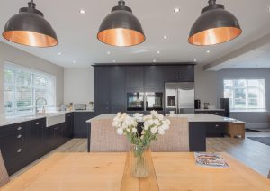 Modern kitchen and dining area with pendant lights, a wooden table, and flowers in a vase.