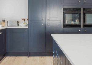 Modern kitchen with navy cabinets, white countertops, and built-in double ovens.
