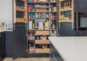 Open kitchen pantry with shelves and drawers filled with food, next to a white countertop.