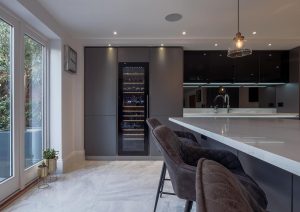 Modern kitchen with a large island, bar stools, wine fridge, and glass doors leading to a garden.