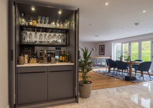 Modern home bar cabinet open in a spacious living room with dining area and large windows.