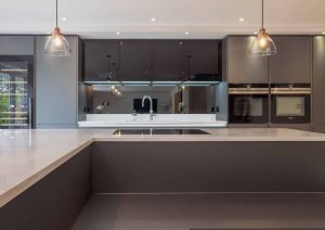 Modern kitchen with dark cabinets, built-in ovens, and a large island with pendant lights above.