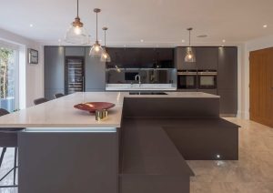 Modern kitchen with dark cabinets, a large island, pendant lights, and marble floors.