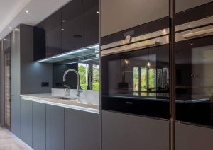 Modern kitchen with sleek black cabinets, built-in oven, and under-cabinet lighting.