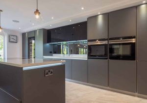 Modern kitchen with dark cabinets, built-in ovens, island, and large windows for natural light.