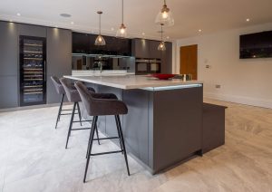 Modern kitchen with a large island, bar stools, dark cabinets, and pendant lights.
