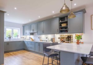 Modern kitchen with grey cabinets, white countertops, and a breakfast bar with two chairs.