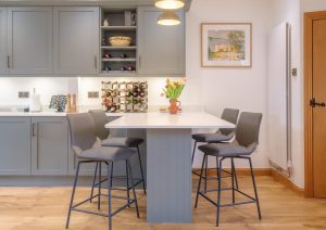 Modern kitchen with grey cabinets, a central island, four stools, and a vase of flowers on the table.