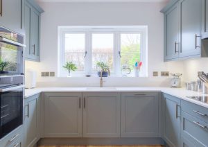 Modern kitchen with light blue cabinets, white countertops, and a window above the sink.